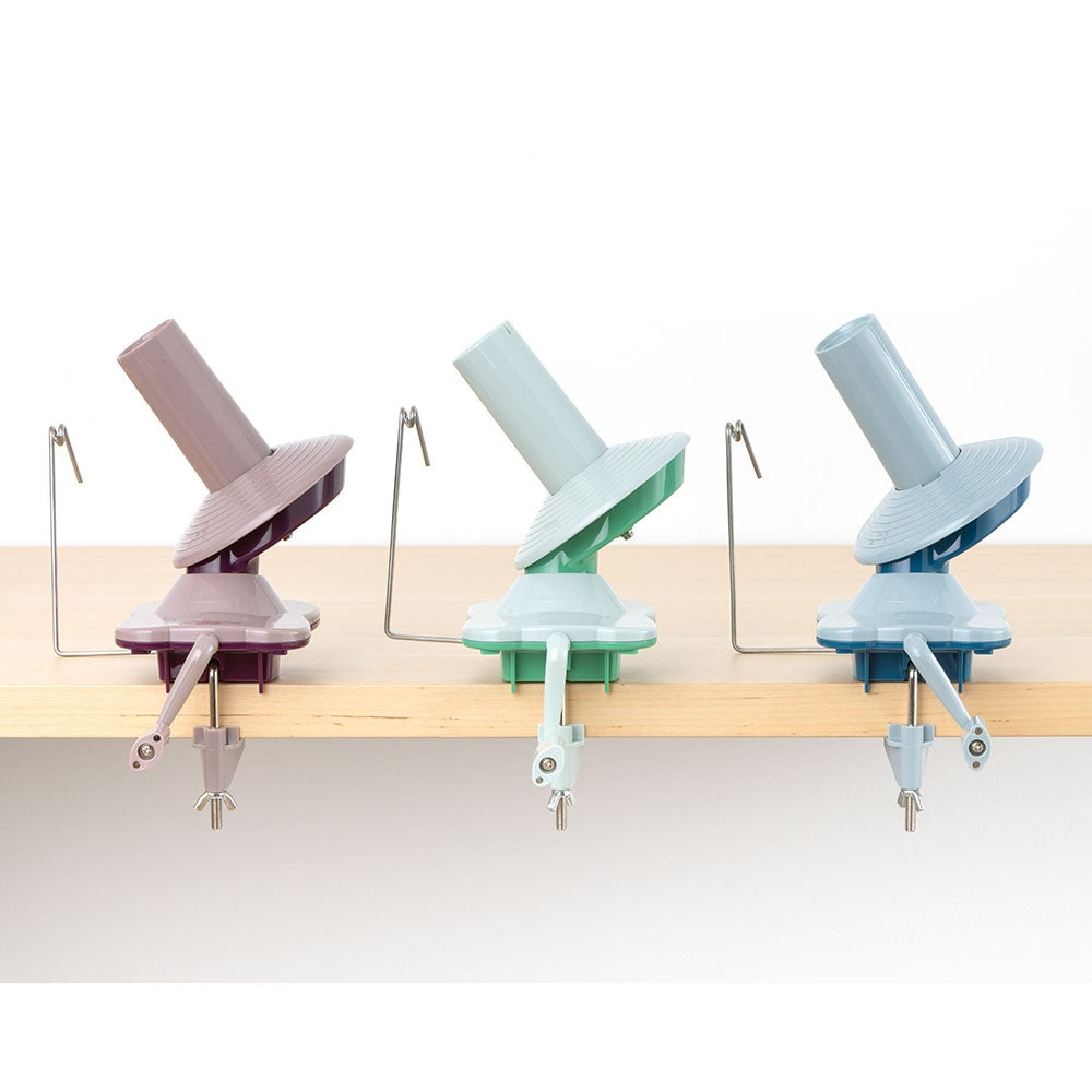Three pastel-colored yarn ball winders clamped to a wooden table edge