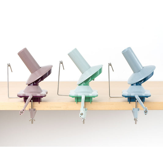Three pastel-colored yarn ball winders clamped to a wooden table edge