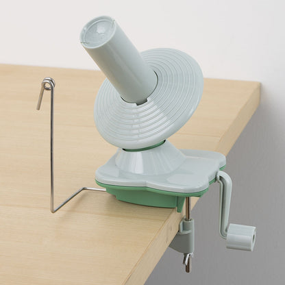 Light green yarn ball winder clamped to wooden table with metal wire guide and hand crank