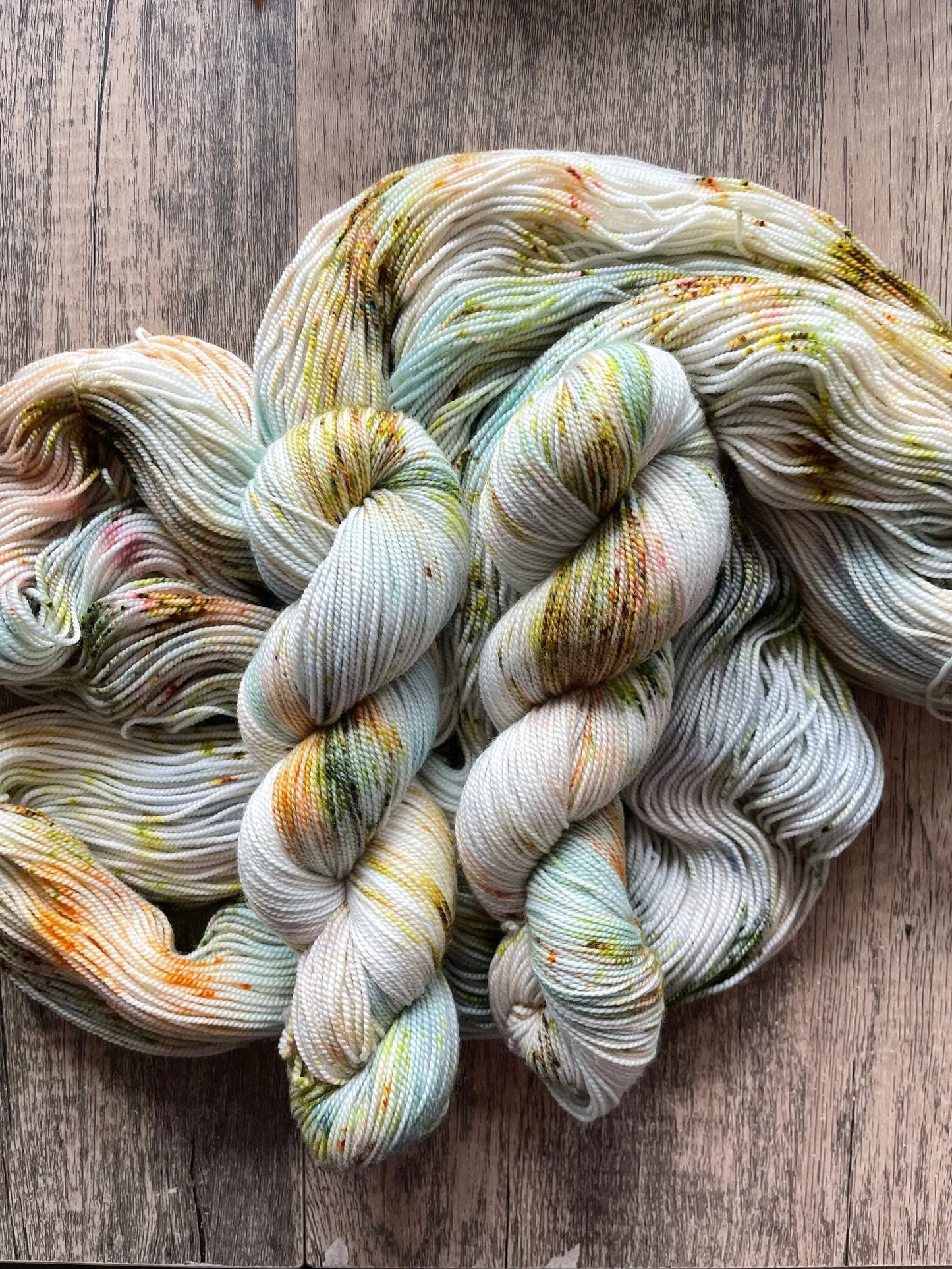 Hand-dyed speckled yarn skeins with pastel green, orange, and brown colors on wooden surface