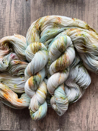 Hand-dyed speckled yarn skeins with pastel green, orange, and brown colors on wooden surface
