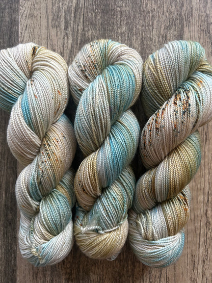 Three skeins of hand-dyed yarn in cream with blue, green, and orange speckles on wood background
