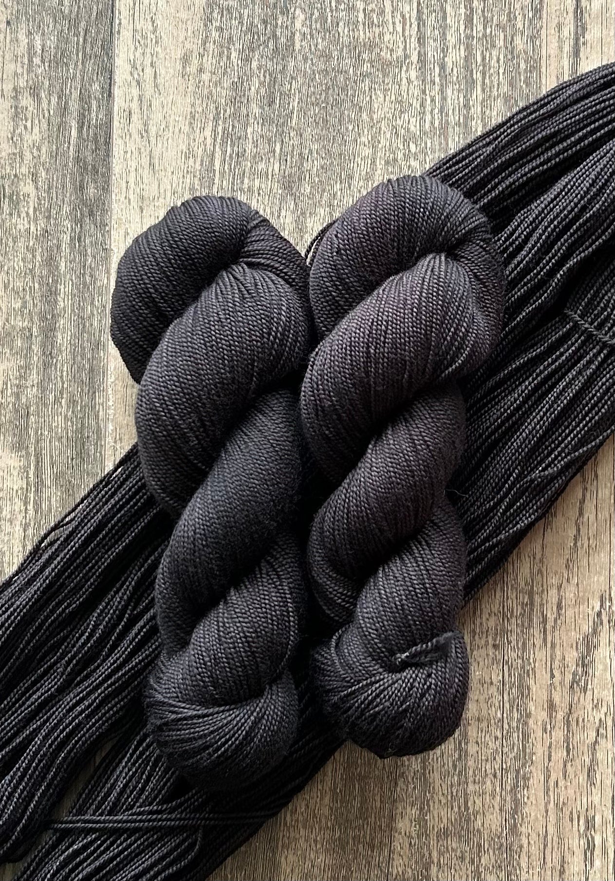 Two skeins of black yarn on wooden surface with stretched yarn strands underneath