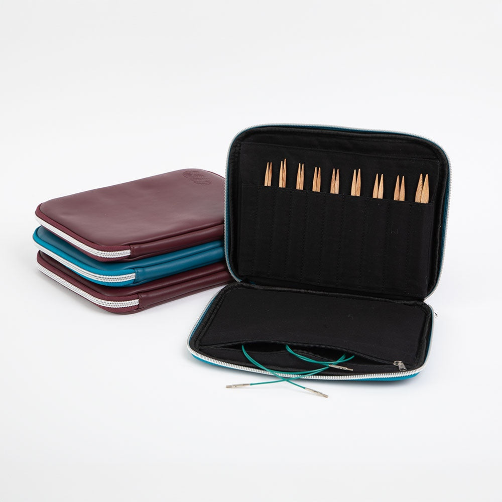 Open knitting needle set with wooden tips in black zippered case beside closed cases in burgundy and teal