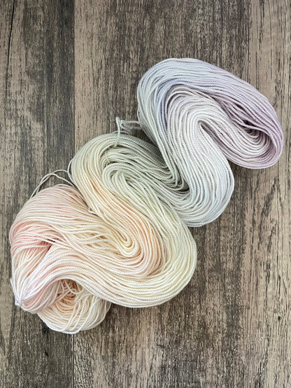Two skeins of pastel hand-dyed yarn in soft peach, green, white, and lavender on wooden background