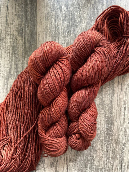 Two skeins of rust-colored yarn on a rustic wooden surface, showing soft, twisted fibers