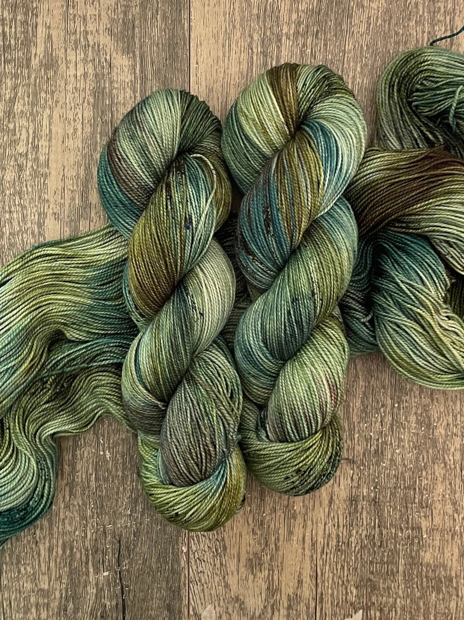 Hand-dyed green and teal variegated yarn skeins on rustic wooden surface