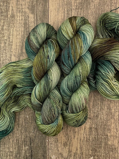 Hand-dyed green and teal variegated yarn skeins on rustic wooden surface