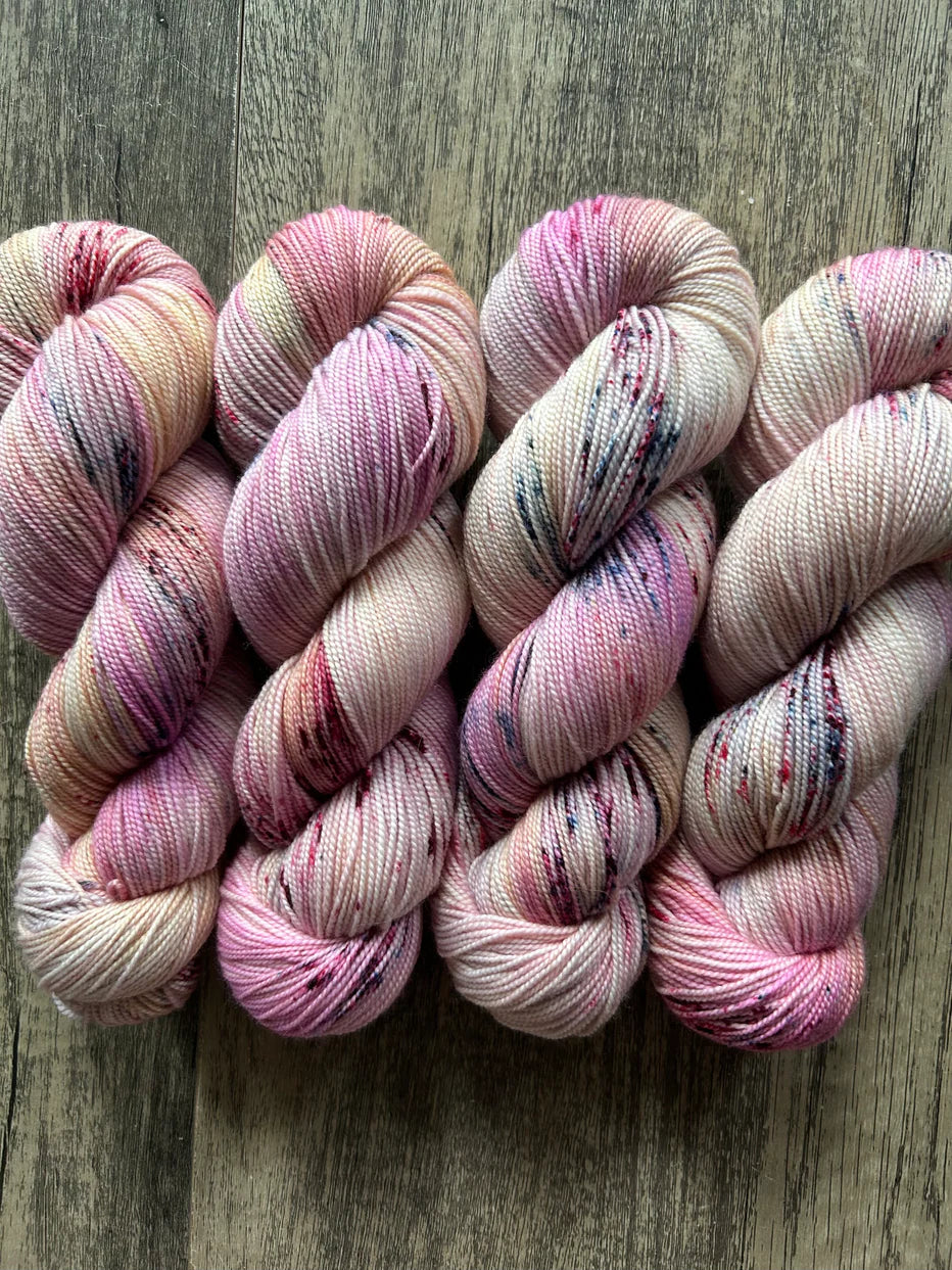 Four skeins of pink speckled hand-dyed yarn on a wooden surface